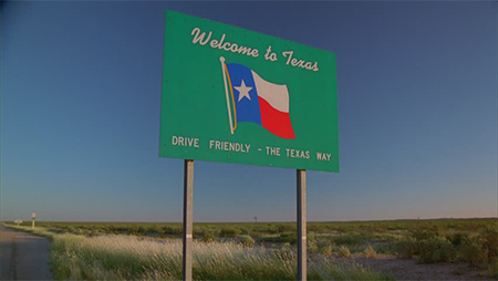 A green sign on the side of the road reads, "Welcome to Texas. Drive friendly - the Texas way."