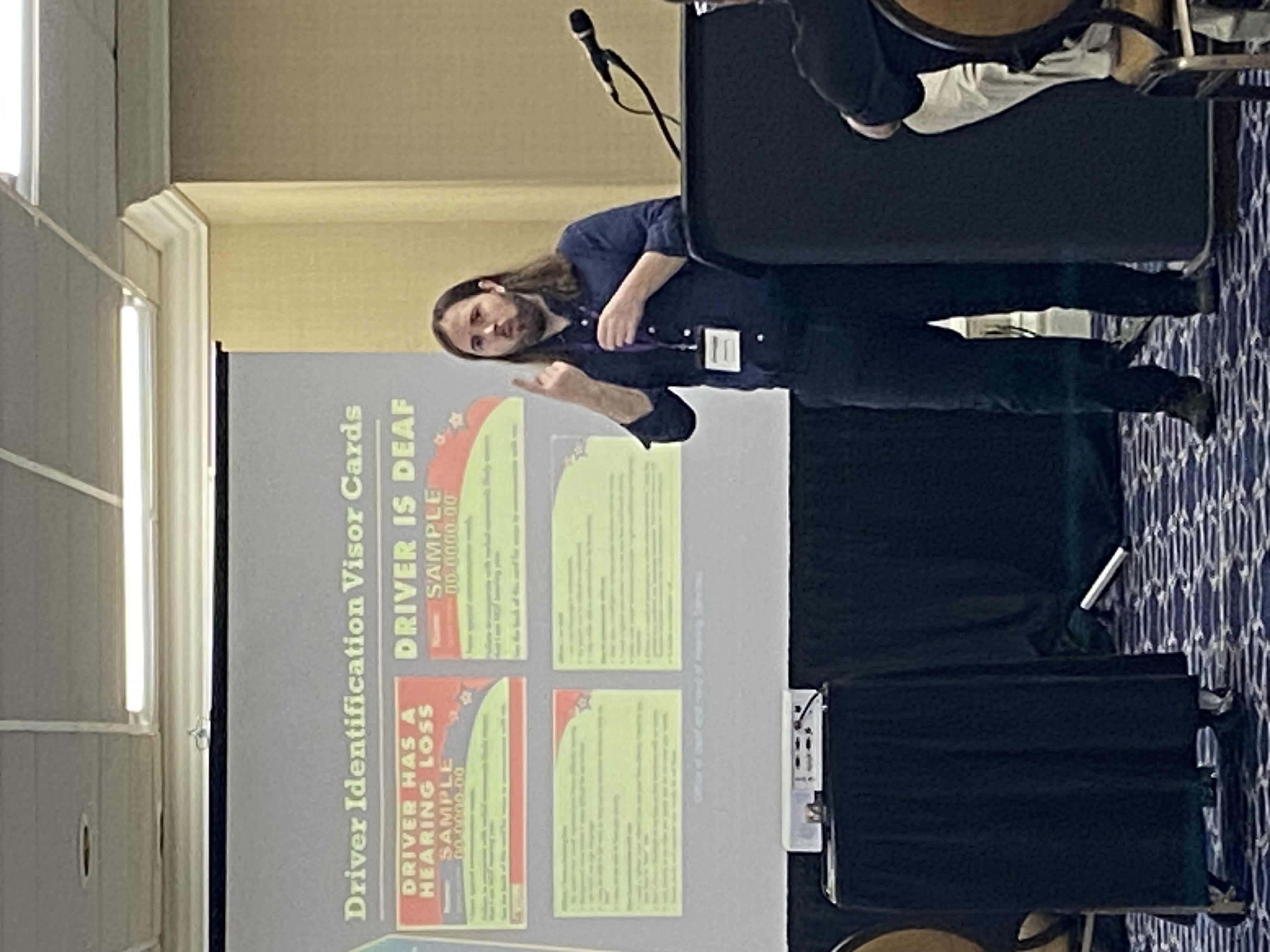 Man presenting to an audience of conference standing in front of a large display screen