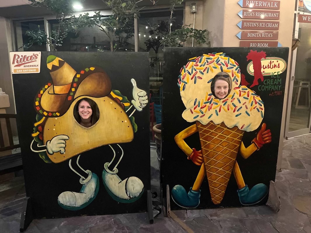 2 people posed behind a taco and an ice cream standing display board